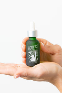 Hand holding a bottle of Activist skincare serum with a white background