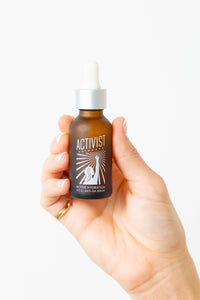 Hand holding a bottle of Activist skincare serum with a white background