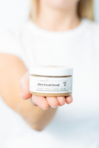 Person holding a jar of Ultra Facial Scrub with a plain background