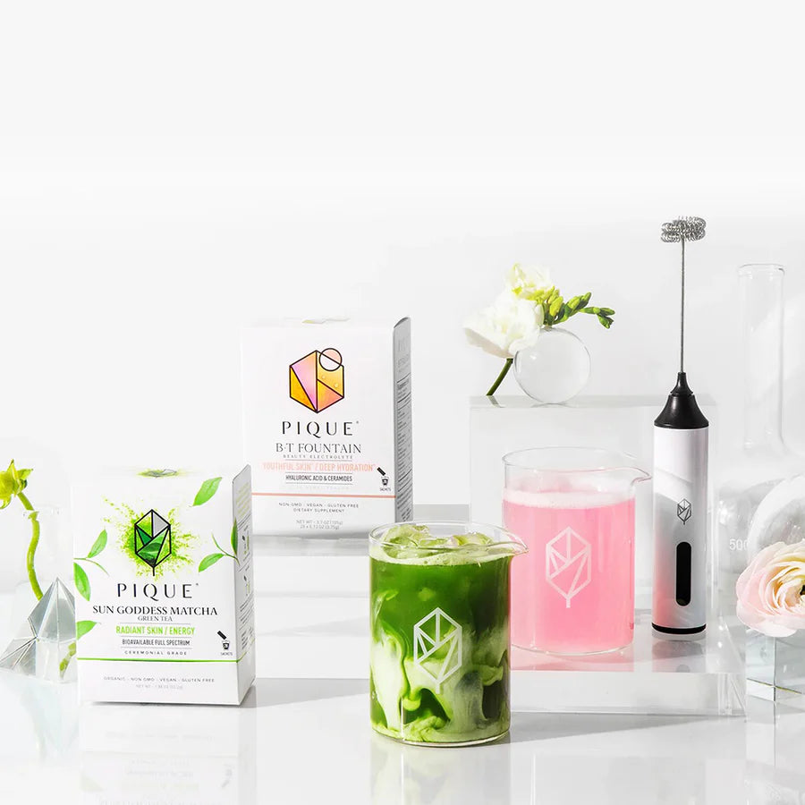 Assortment of Pique Tea products, including matches and pink drink mix, with a whisk and flowers. Bright, fresh, and modern aesthetic.