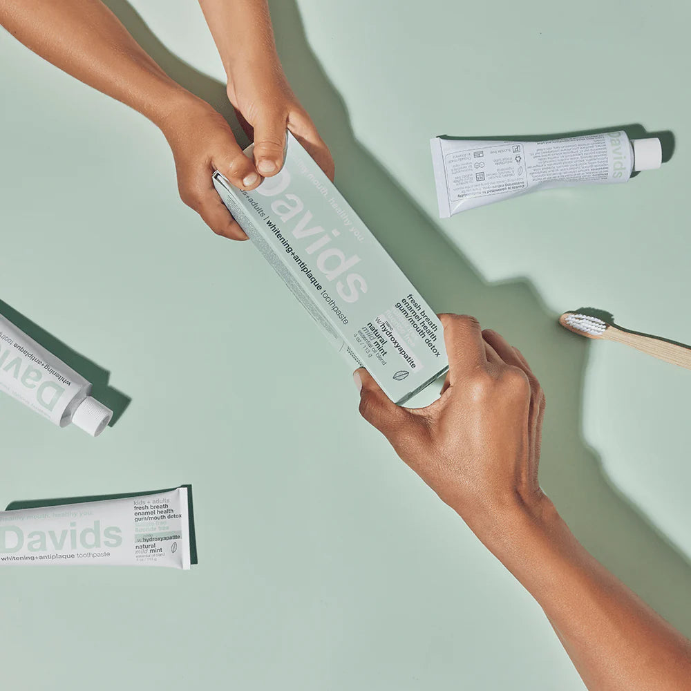 Two hands holding a box of Davids toothpaste against a light green background.