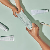 Two hands holding a box of Davids toothpaste against a light green background.