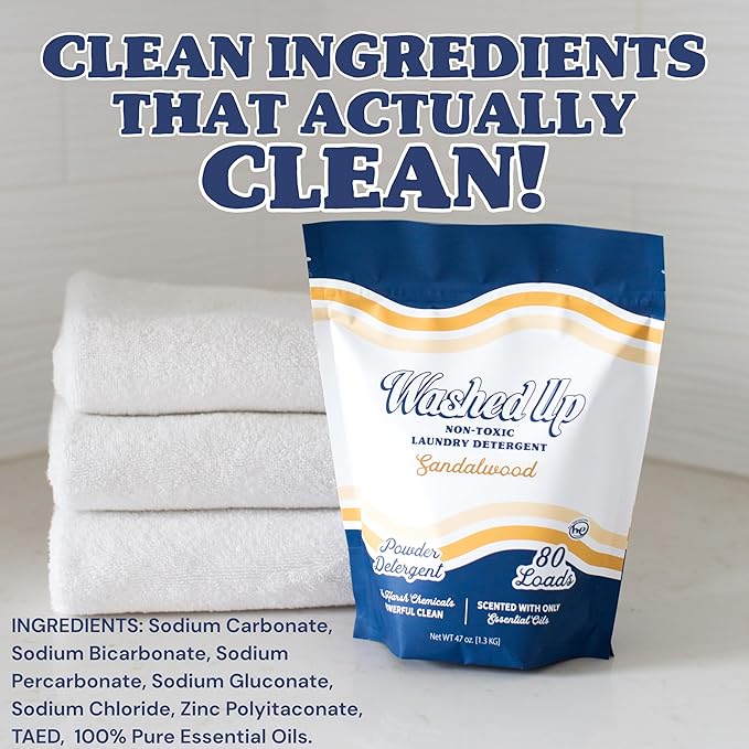 Laundry detergent bag labeled 'Washed Up' with white and gold design, placed on a counter next to folded white towels. Text reads 'Clean ingredients that actually clean!' and lists ingredients below.