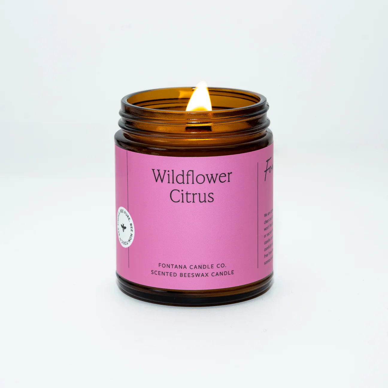 A photo of a lit Wildflower Citrus scented candle with a pink label, made by Fontana Candle Co. in a brown jar.