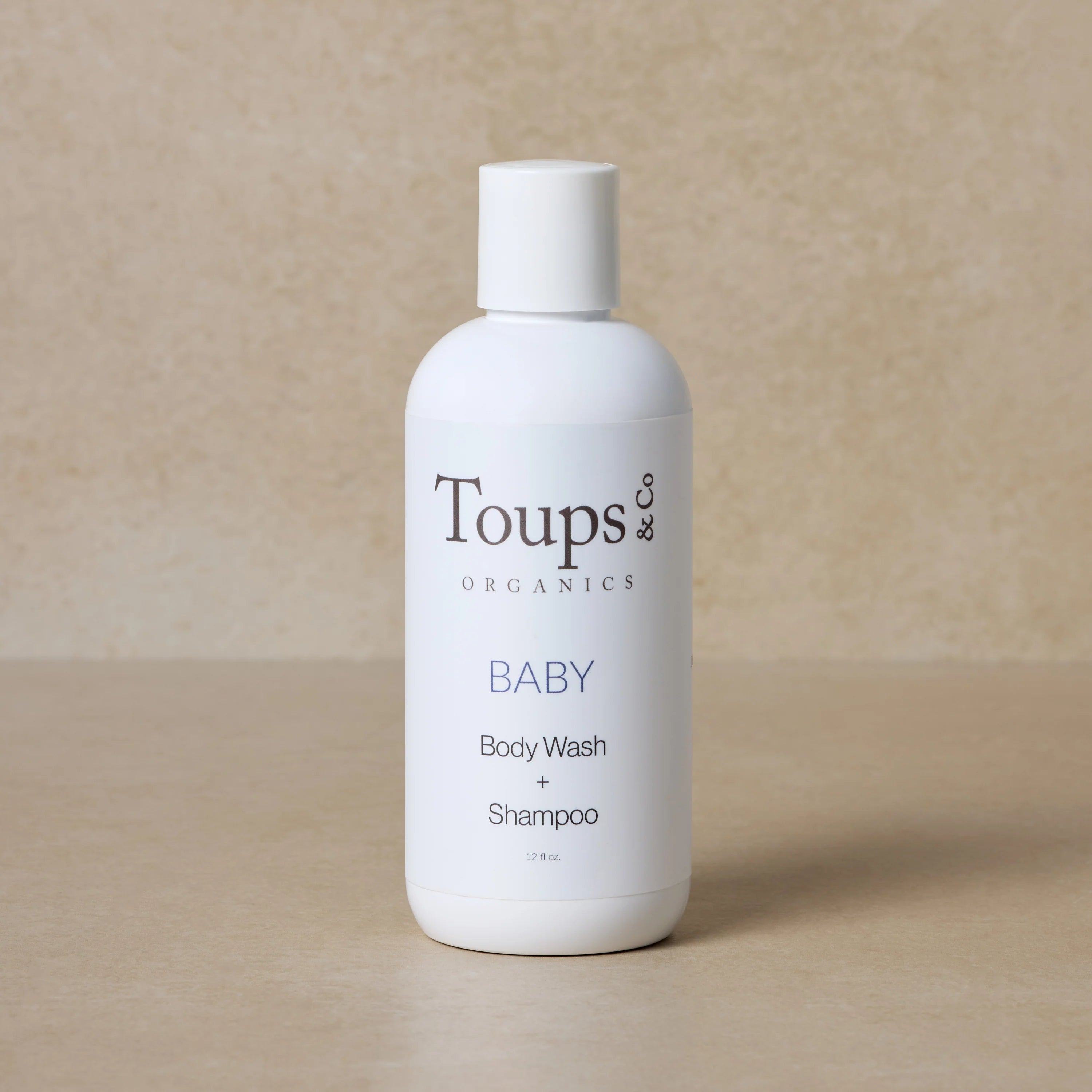 A white bottle with a label that reads 'toups organics baby body wash shampoo' in a textured background.