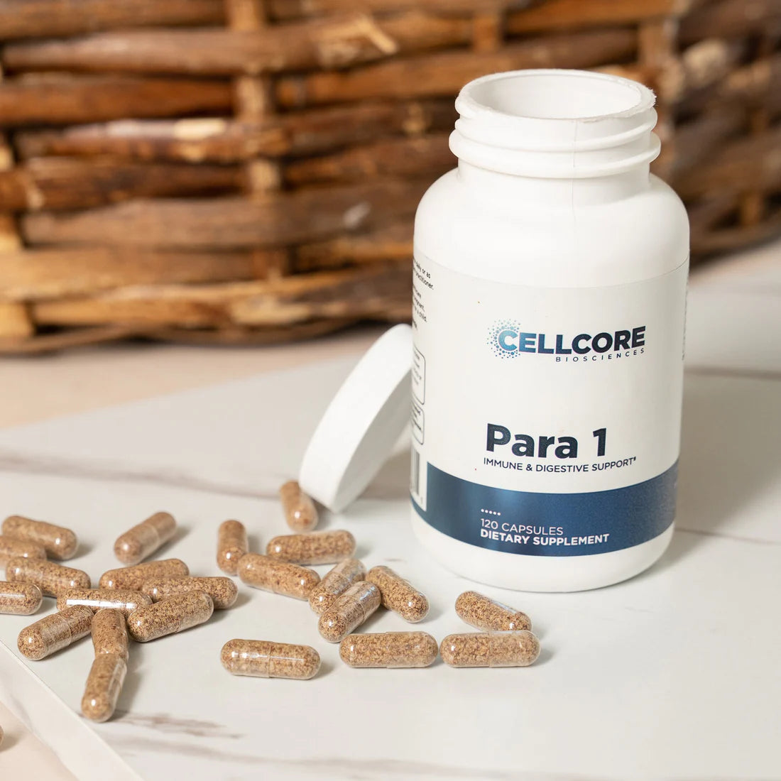 A bottle of 'Para 1' dietary supplement by CellCore, with capsules spilling out in front of the bottle, on a white surface with a woven basket in the background.
