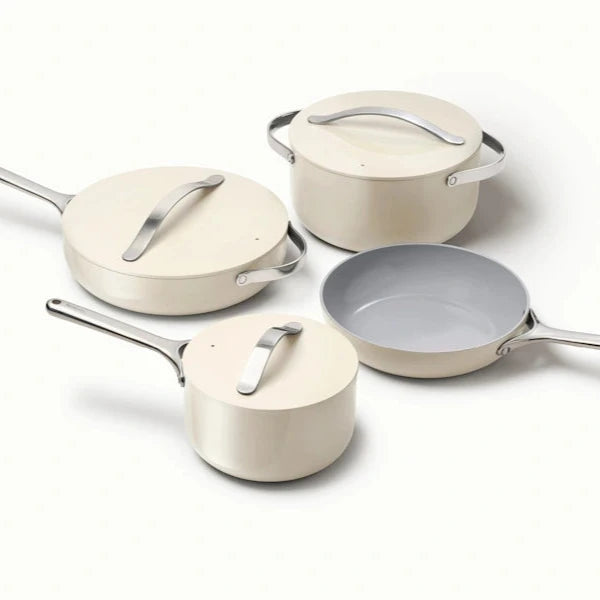 Four cream-colored cookware pieces with silver handles are arranged: a saucepan, a frying pan, and two covered pots. Minimalist and sleek design.