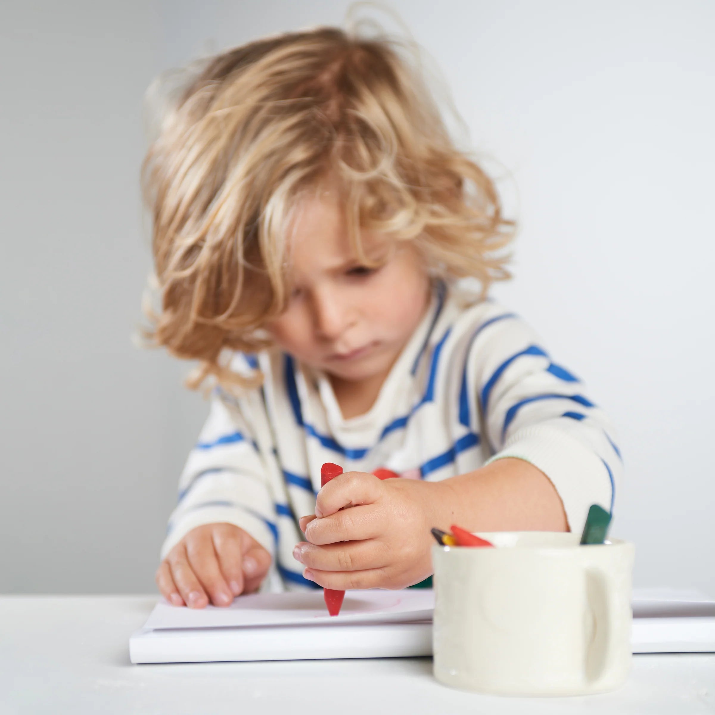 Child coloring with crayons on a white surface
