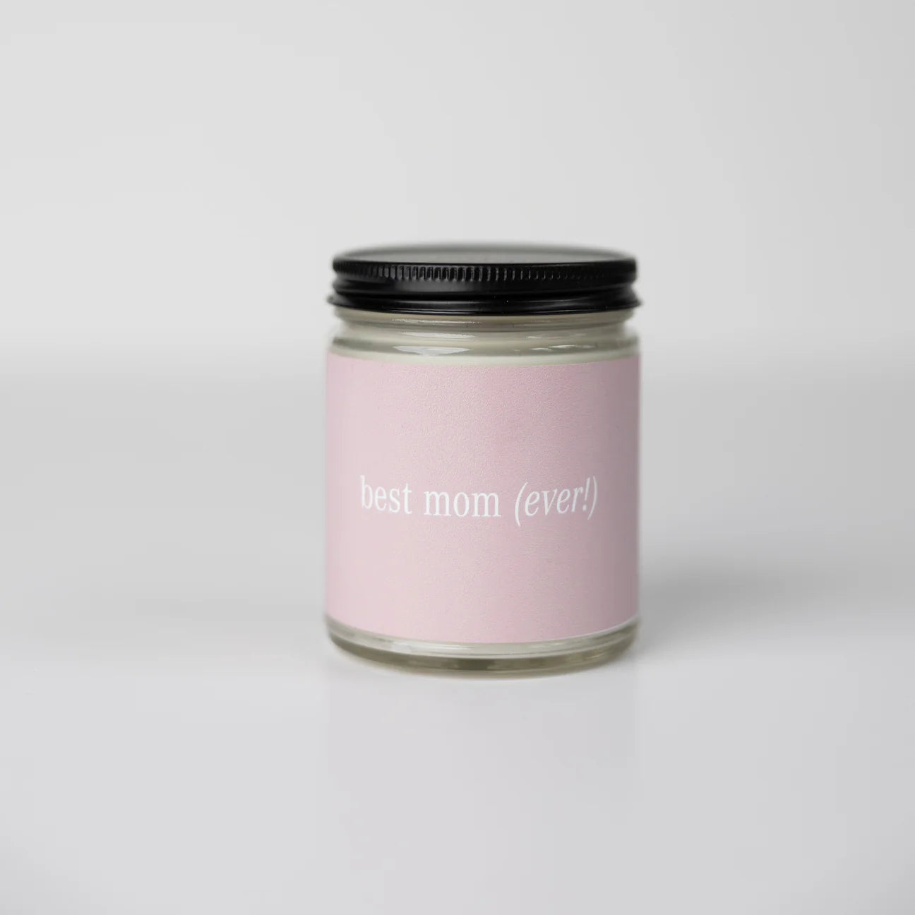 A soy candle in a black metal tumbler with a pink label reading 'best mom ever'.