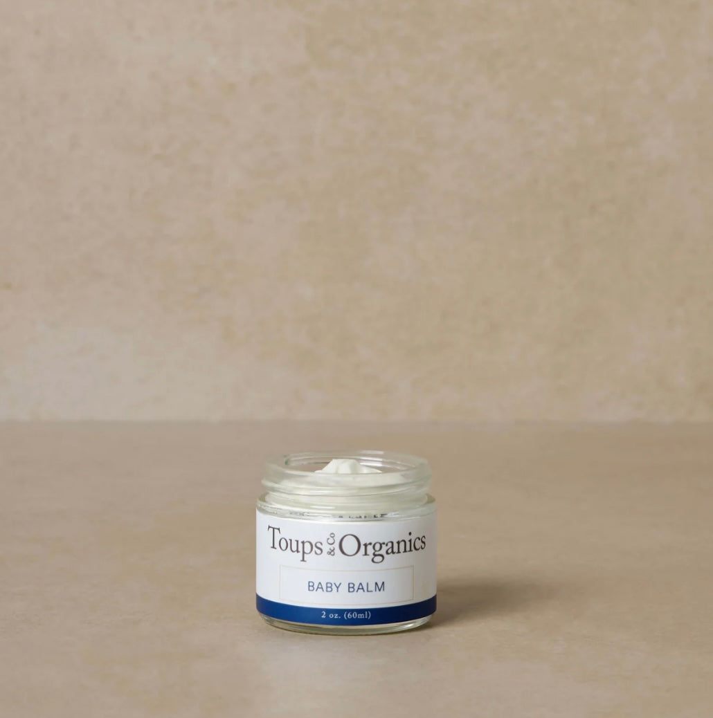 Jar of Toups Organics baby balm on a beige background