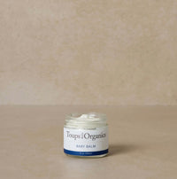 Jar of Toups Organics baby balm on a beige background