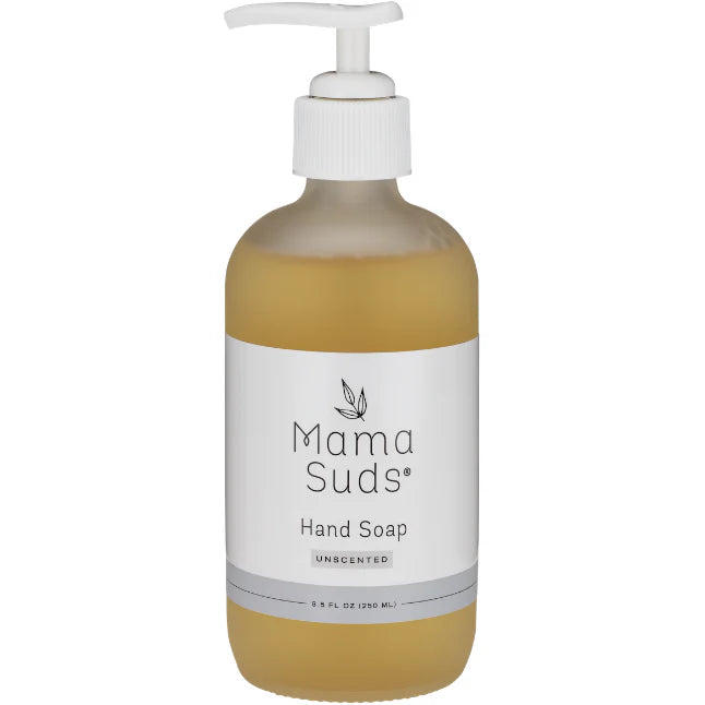 A glass bottle of liquid hand soap with a pump dispenser, labeled 'MamaSuds', placed on a wooden surface with a bright kitchen background.