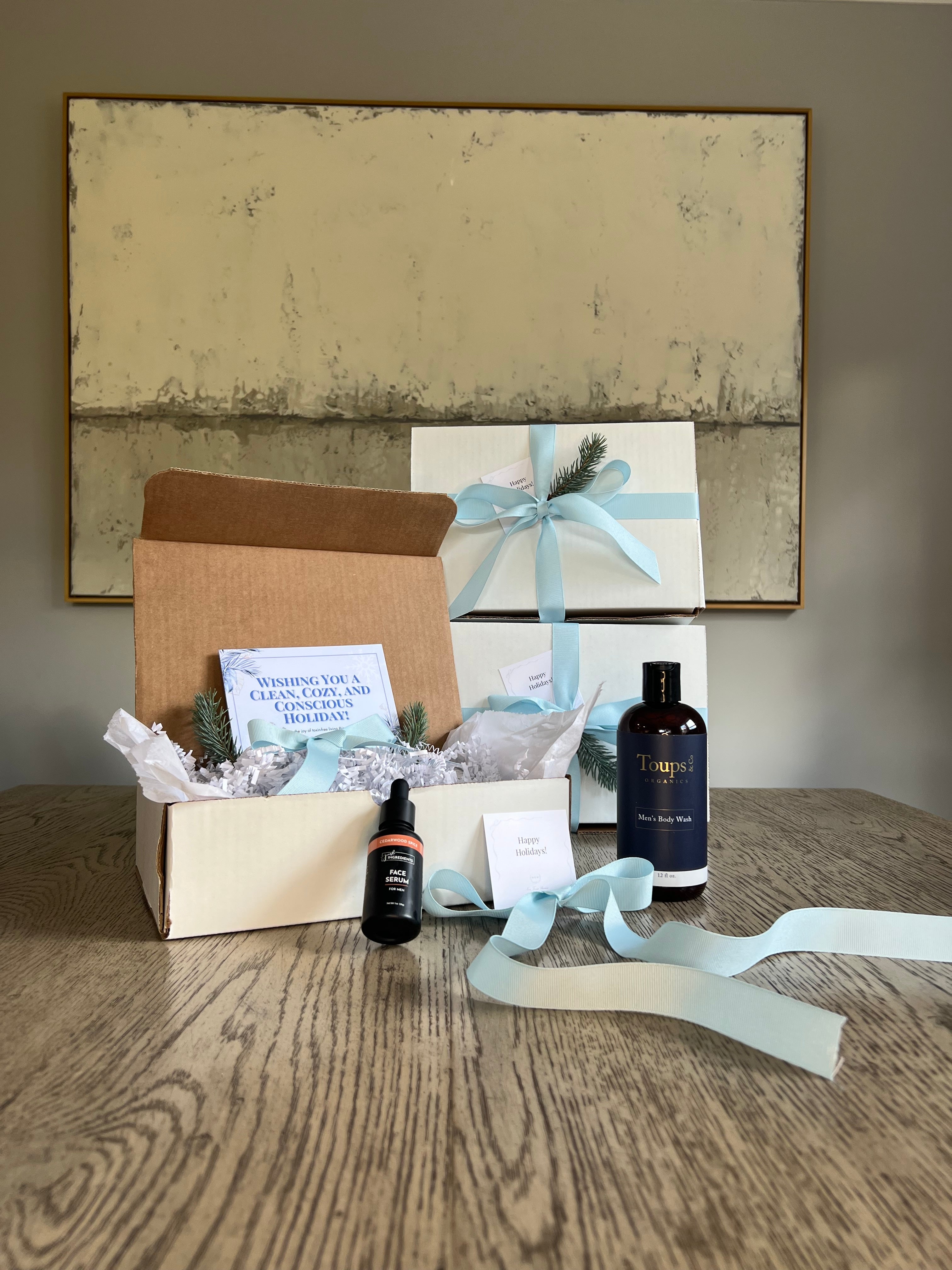 Open gift box with products on a wooden surface, featuring a decorative ribbon and cards.
