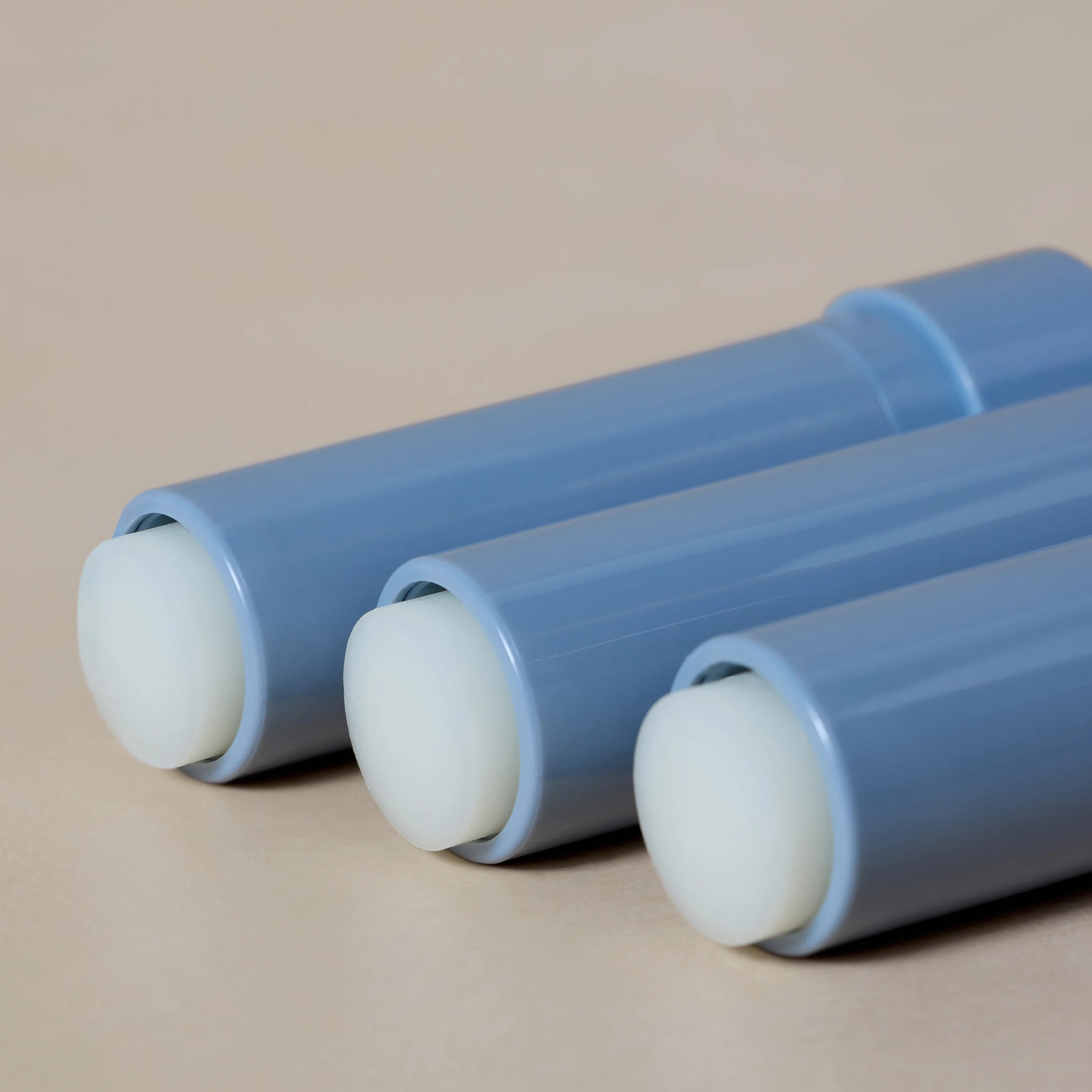 Three blue lip balms with white caps on a beige background
