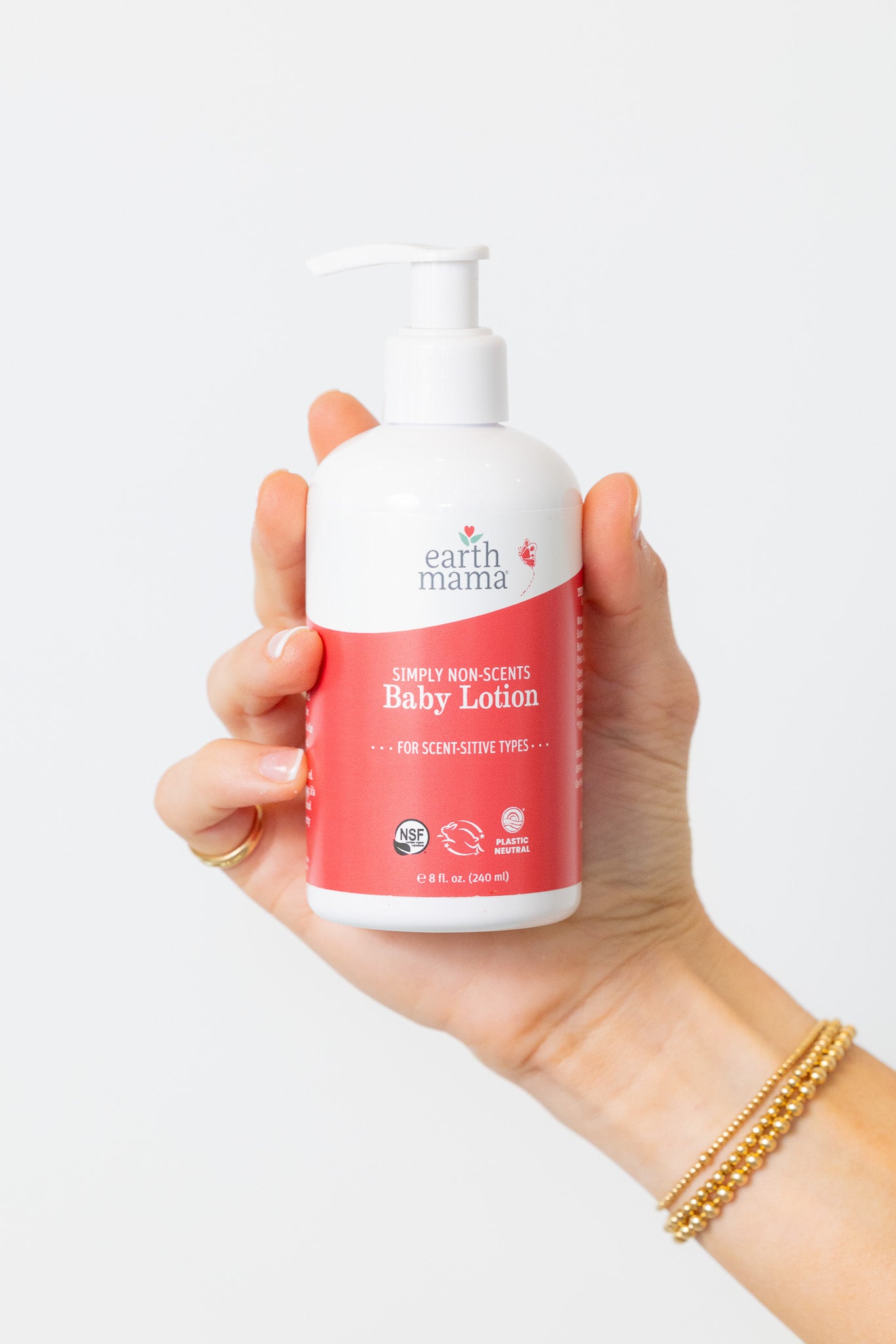 Hand holding a bottle of Earth Mama Angel Baby Lotion against a white background