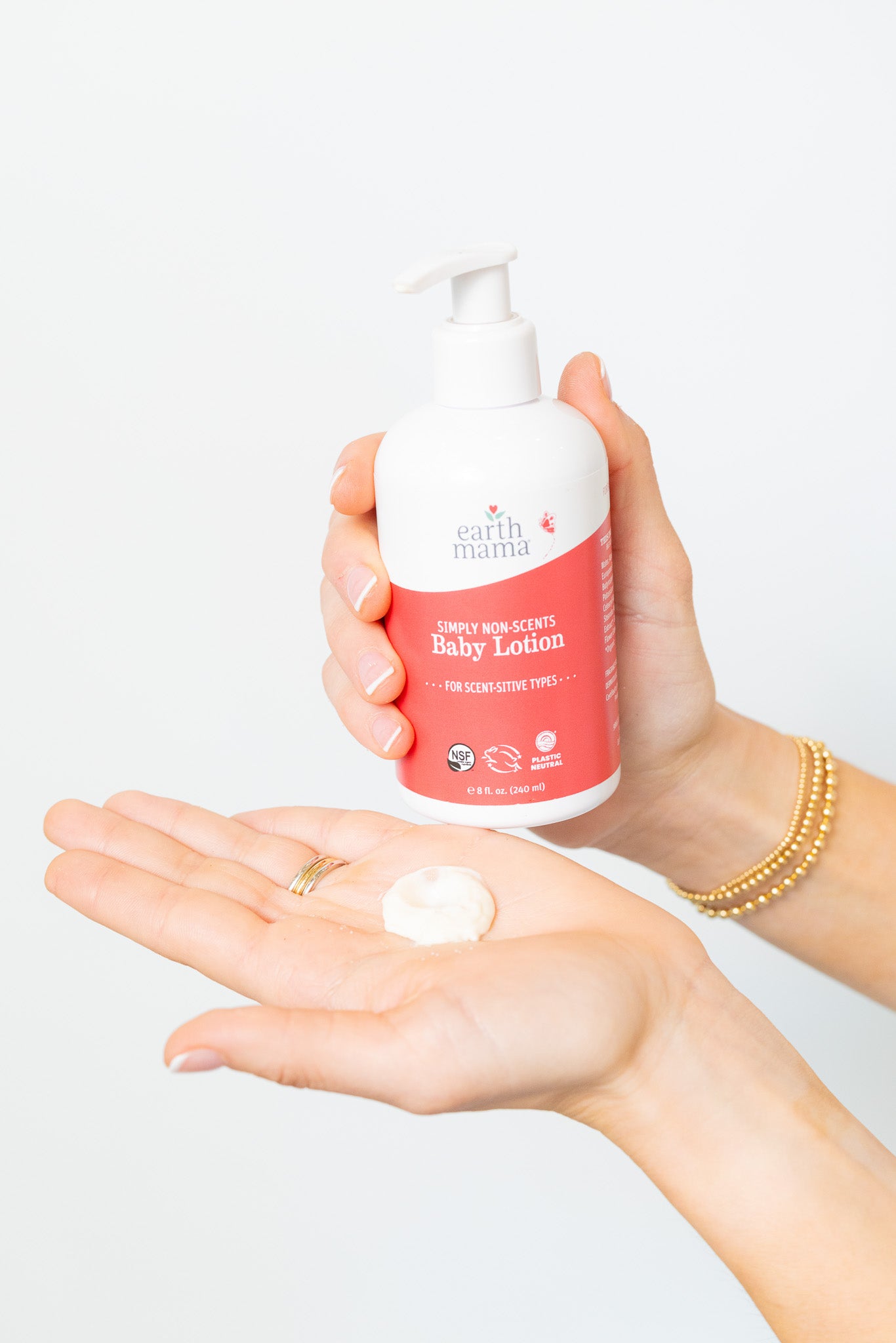 Person holding a bottle of baby lotion with a small amount on their palm against a white background