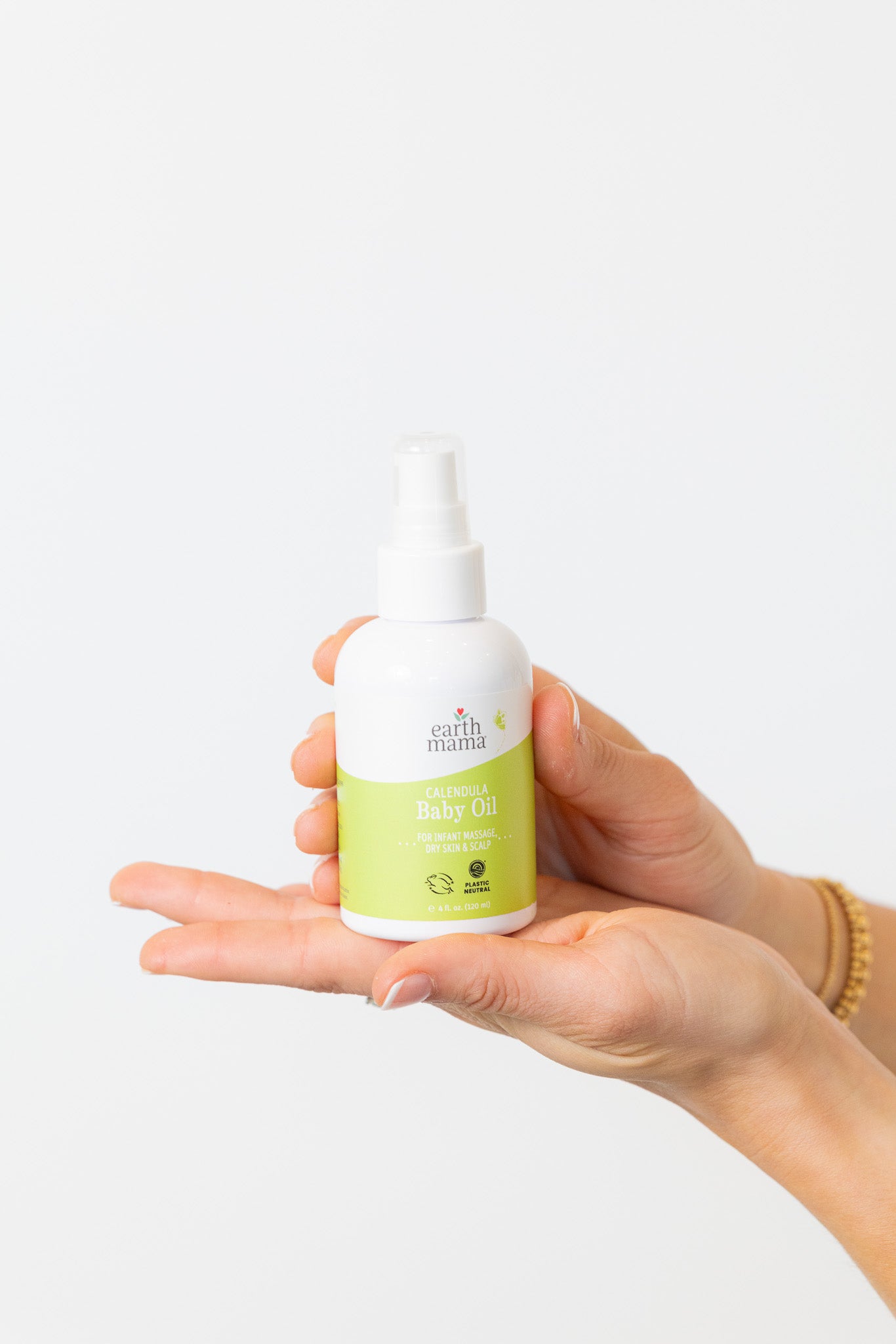 Hand holding a bottle of Earth Mama Angel Baby Oil against a white background