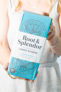 A person holding a box of Root & Splendor laundry detergent with a blue and green label.