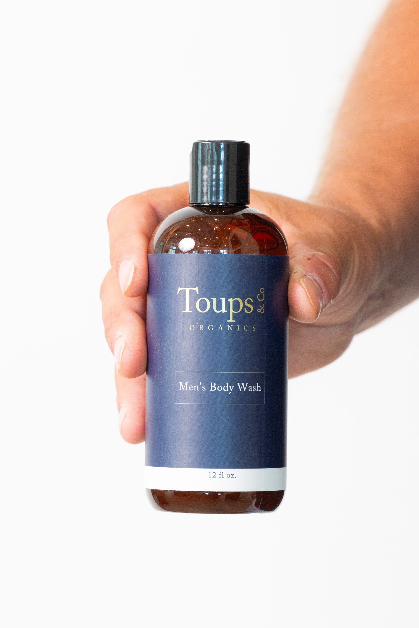 Hand holding a bottle of Toups Organics Men's Body Wash against a white background