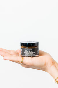 Hand holding a jar of honey cream mask against a white background