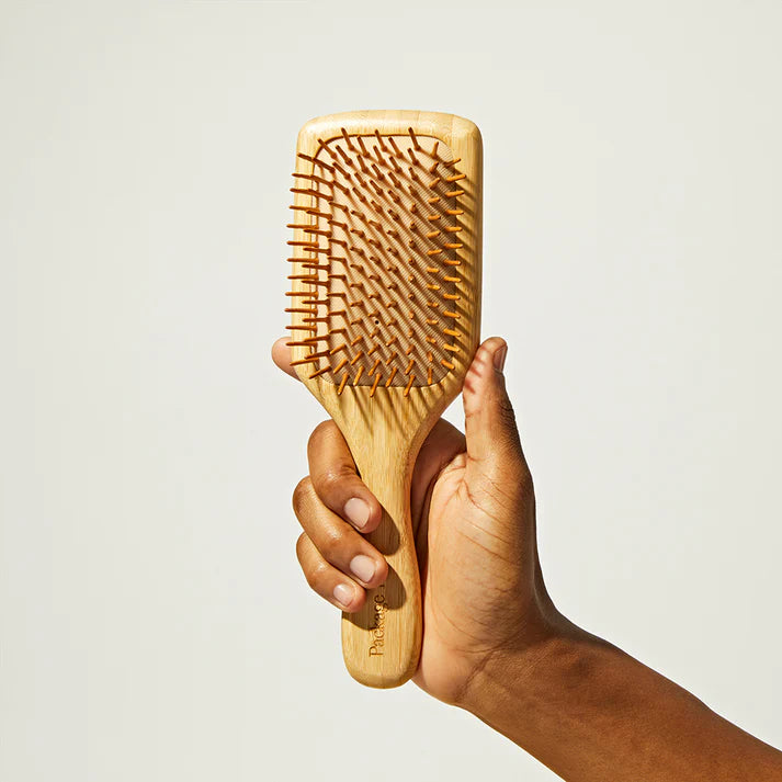 Hand holding a wooden hairbrush against a plain background