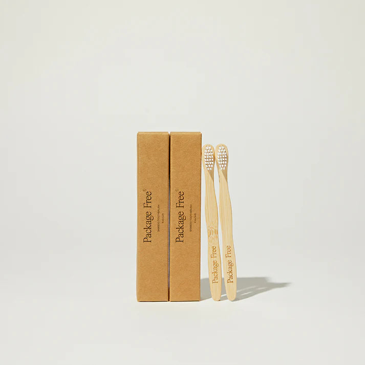 Two bamboo toothbrushes with a cardboard box labeled 'Package Free' on a light gray background.