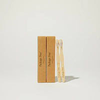 Two bamboo toothbrushes with a cardboard box labeled 'Package Free' on a light gray background.