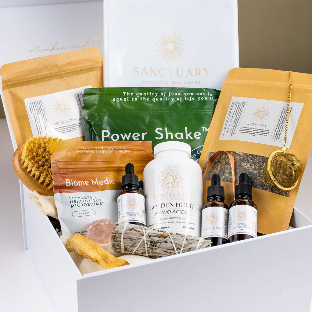 A wellness gift box containing herbal teas, supplements in bottles, a wooden brush, sage bundle, a gold tea infuser, and bath items, evoking relaxation.