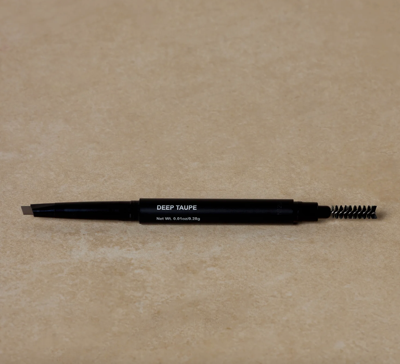A black eyebrow pencil labeled "Deep Taupe" lies on a beige surface. One end has a slanted pencil tip, and the other a spoolie brush for grooming.
