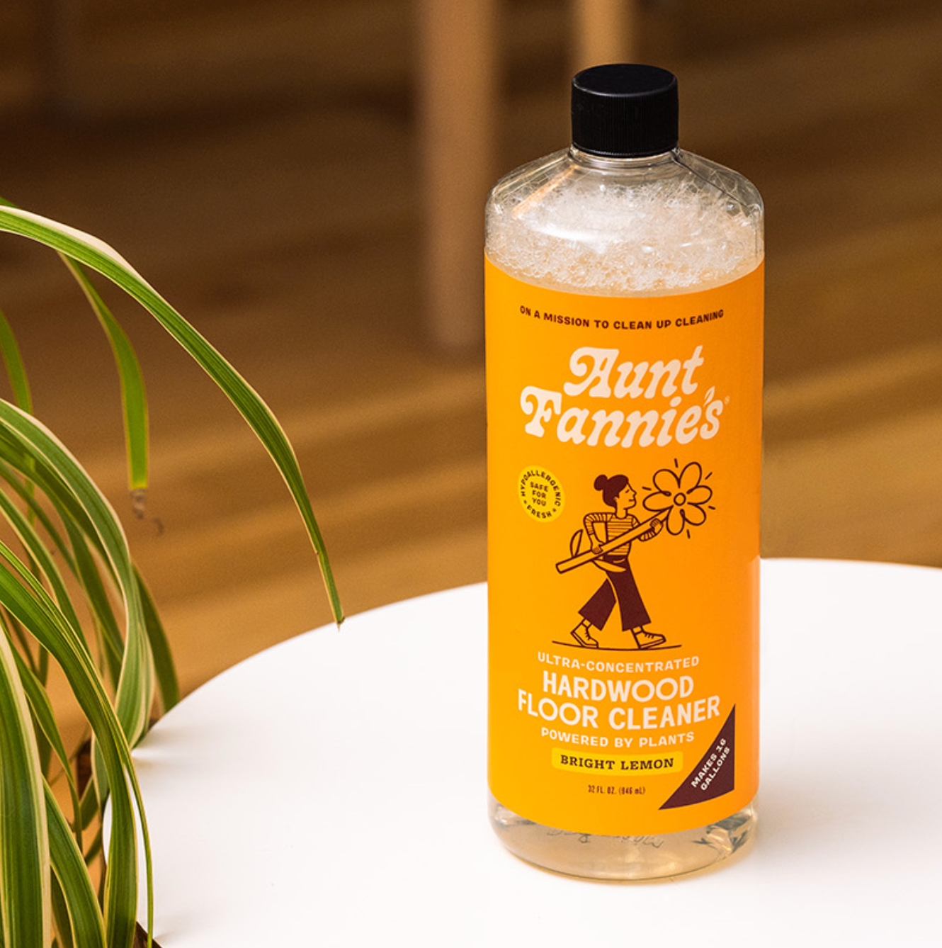 A bottle of Aunt Fannie's Hardwood Floor Cleaner in Bright Lemon scent, placed on a table with a plant in the background.
