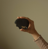 A hand holding a black nephrite gua sha tool with the brand name 'Toupé' visible on it.