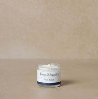 A small clear jar with a white lid labeled 'Toups & Organics Sun Balm' containing a yellowish solid substance, likely the natural sun balm mentioned in the product description.