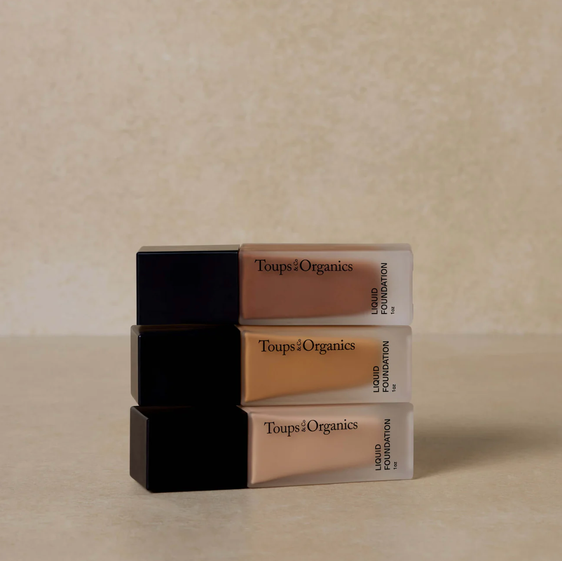 Stack of Toups Organics liquid foundation bottles on a beige background