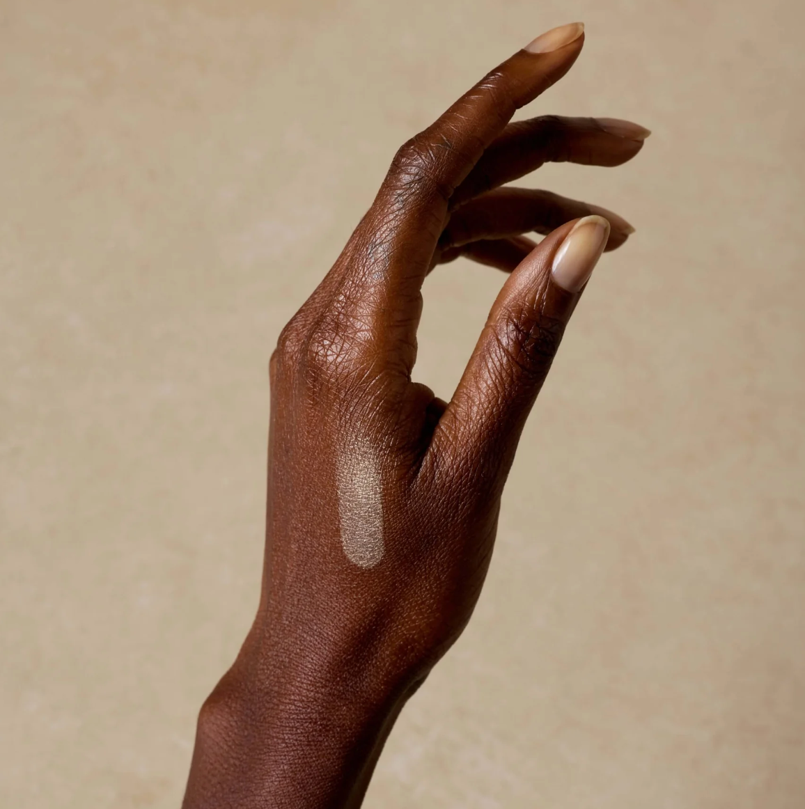 Hand with dark skin and beige nail polish against a beige background