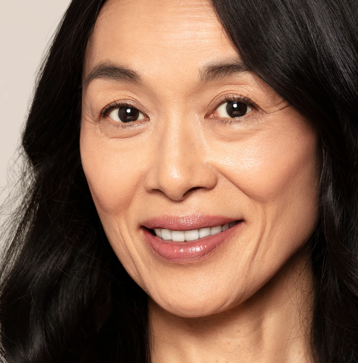Close-up of a woman with dark hair and a neutral background