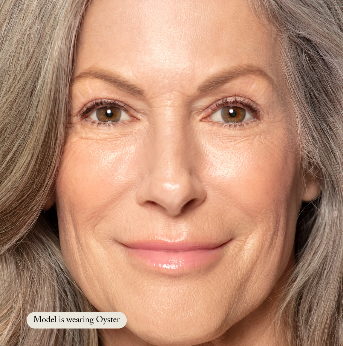 Close-up of a woman with gray hair wearing makeup, with a label indicating she is wearing 'Oyster'.