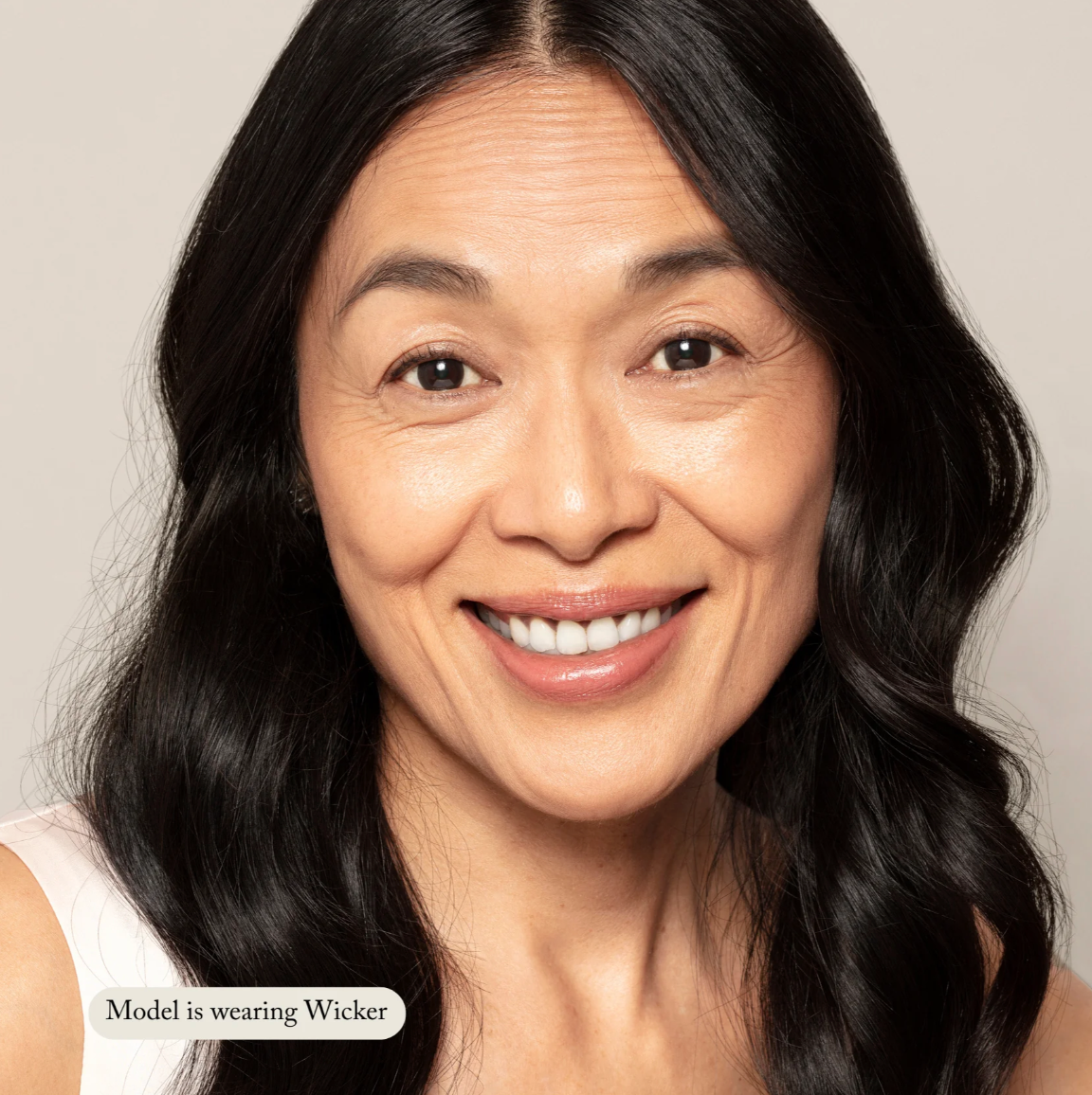 Woman with long dark hair wearing a beige top against a neutral background
