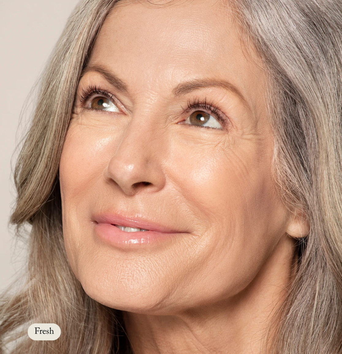 Close-up of a woman with gray hair and a neutral expression against a beige background