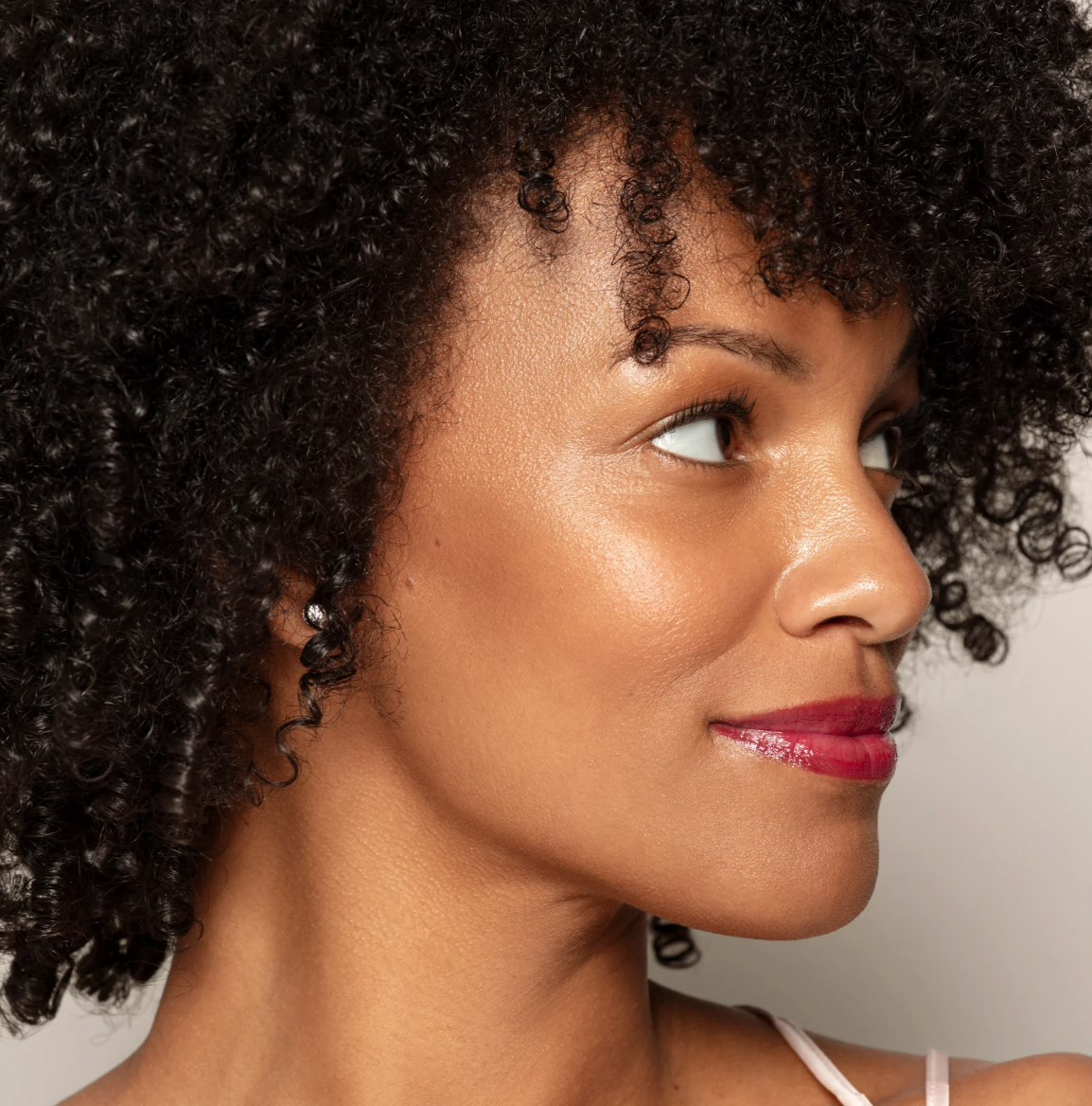 Woman with curly hair wearing a white top against a neutral background