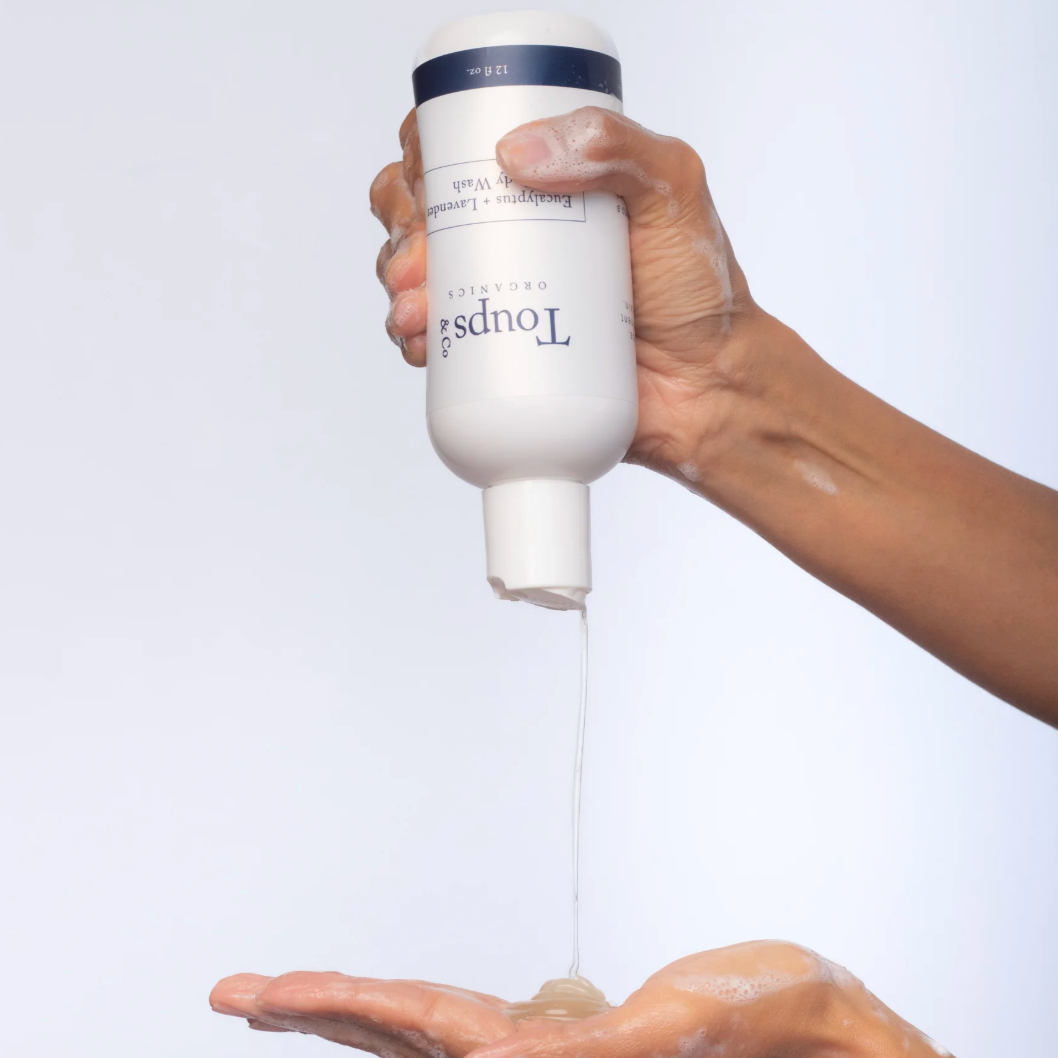 Hand holding a bottle of Toupes skincare product with white foam being dispensed onto a palm.