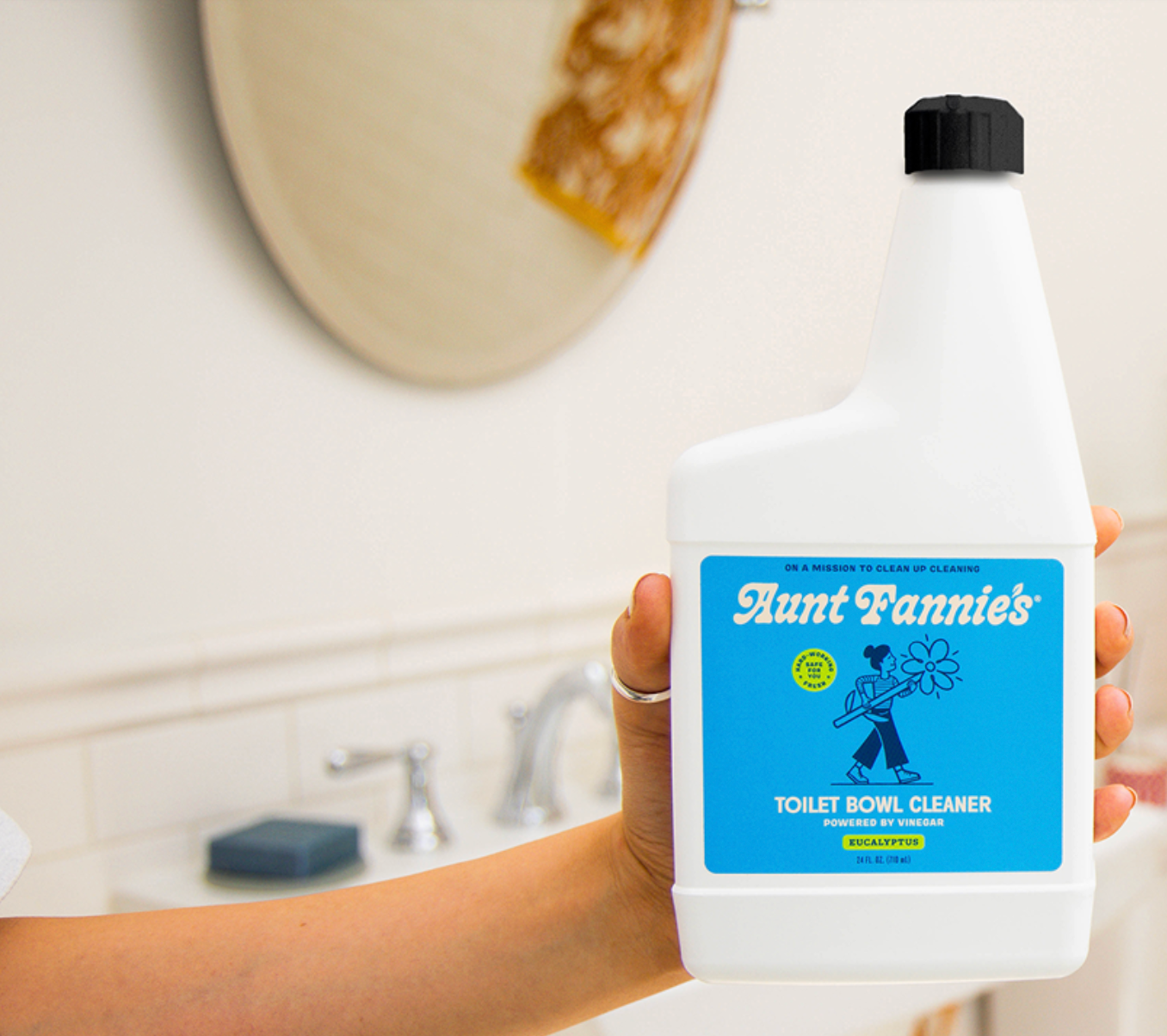 Person holding a bottle of Aunt Fannie's Toilet Bowl Cleaner in a bathroom setting.