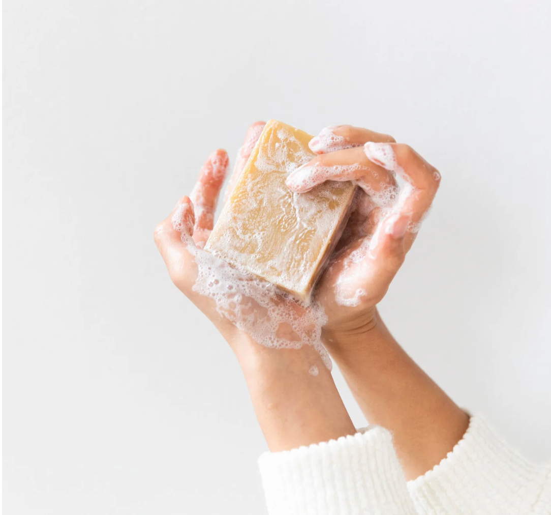 Hand holding a bar of soap with lather against a light background