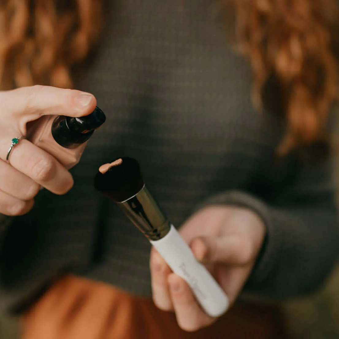A person holding a bottle of liquid foundation with a applicator sponge.