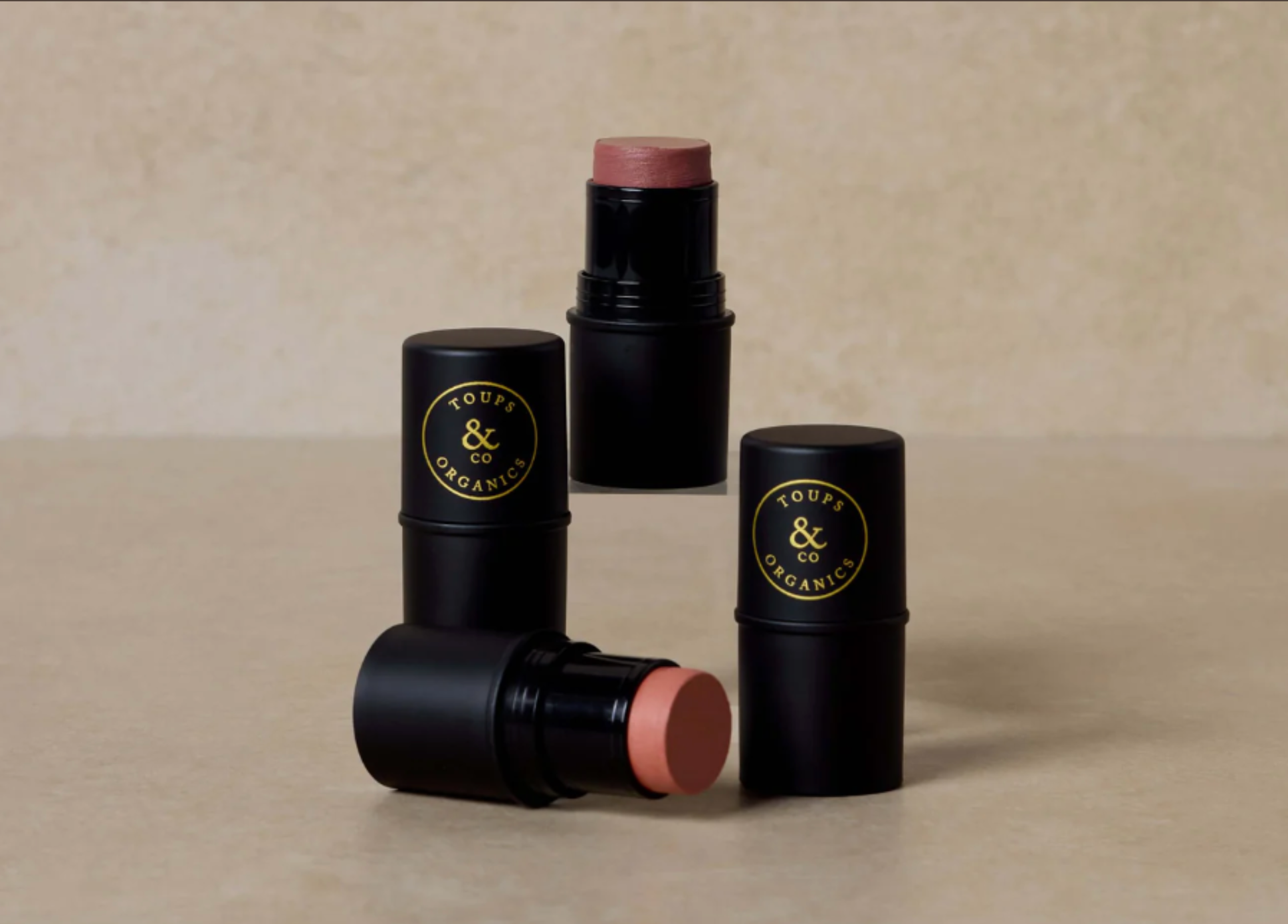 Four black cosmetic sticks with visible brand logo on a beige background