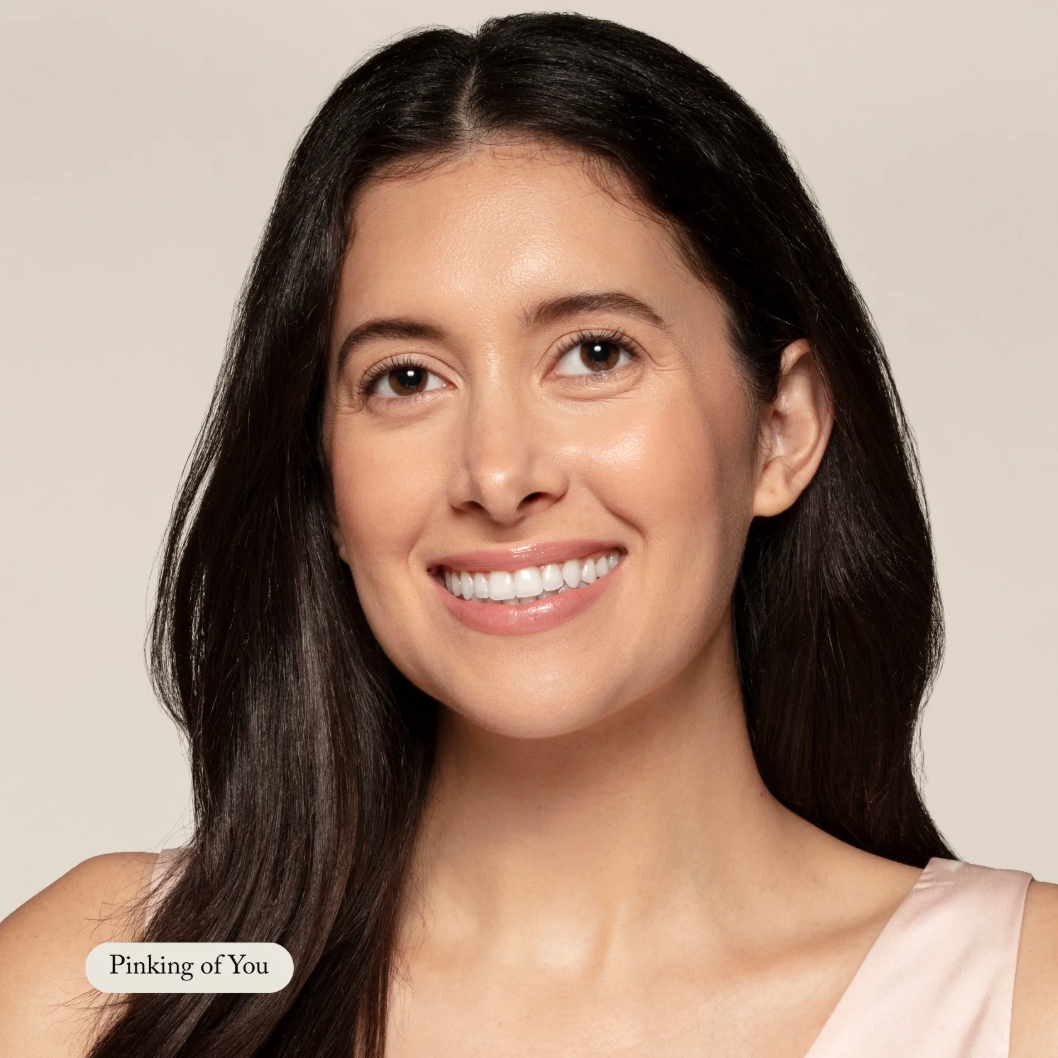 Woman with long dark hair smiling against a plain background