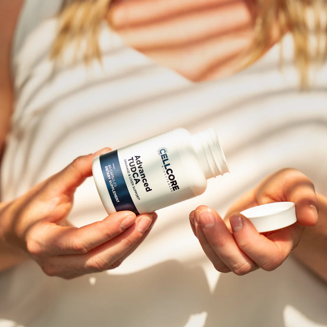 A bottle of Advanced TUDCA supplement held in a person's hands, with the supplement name and dosage information visible on the label.