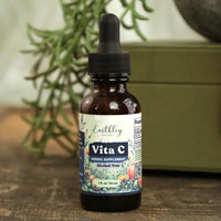 Bottle of Earthly Vita C supplement with dropper on a wooden surface with plants in the background