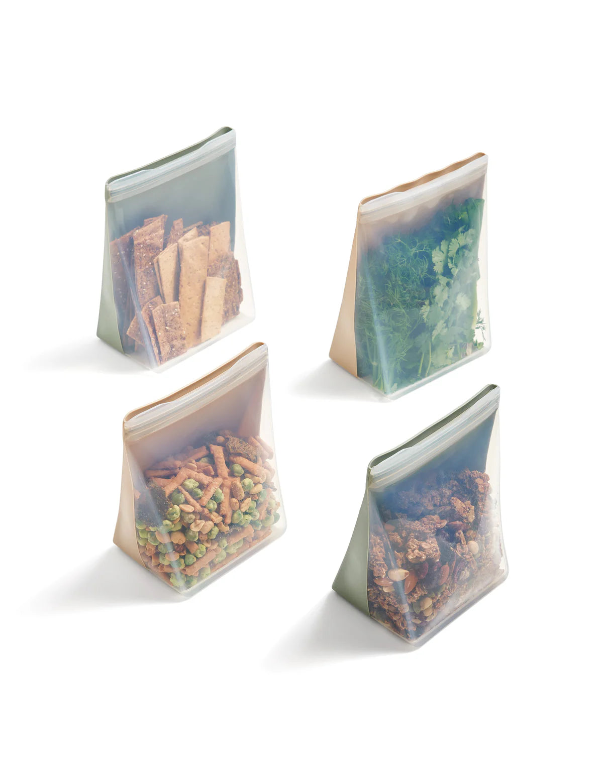 Four transparent, reusable silicone bags are filled with snacks: crackers, leafy greens, small treats, and granola. They stand upright on a white surface.