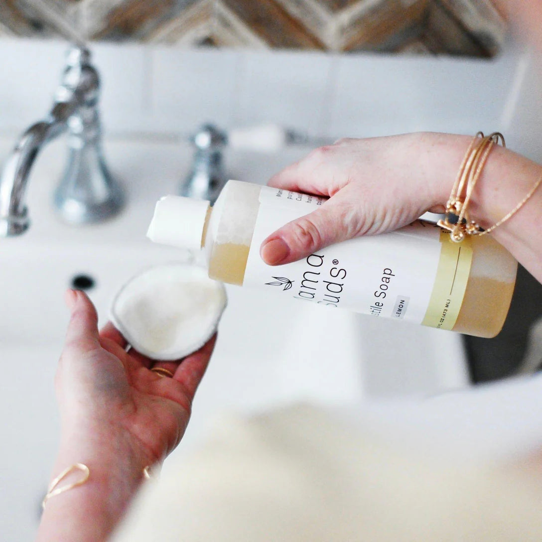Person holding a bottle of baby soap with a washcloth over a sink.