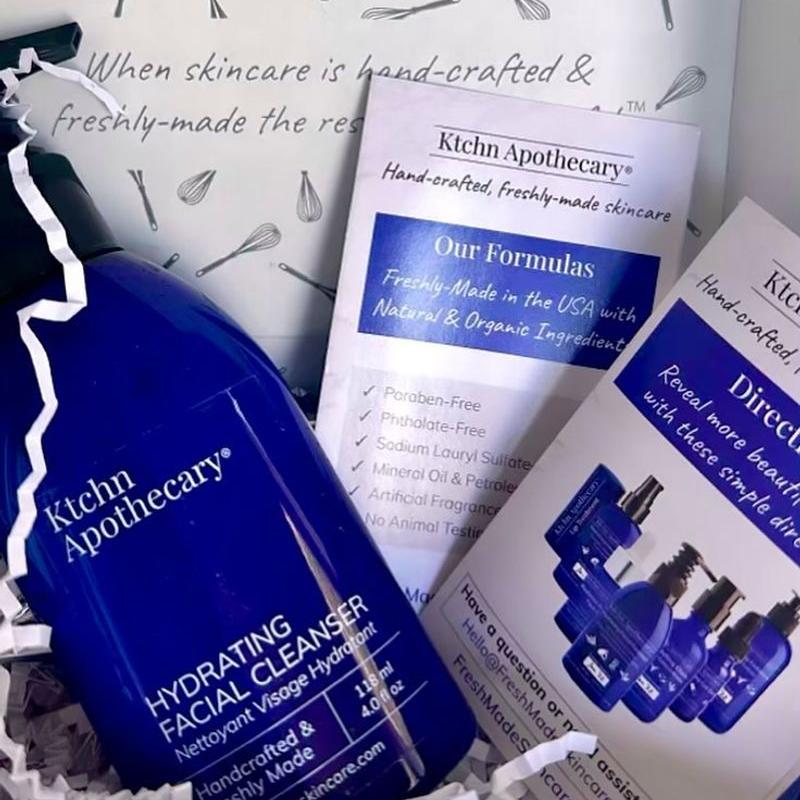 Blue bottle of Kitchen Apothecary Hydrating Facial Cleanser amidst informational cards and packing paper, emphasizing handcrafted skincare.
